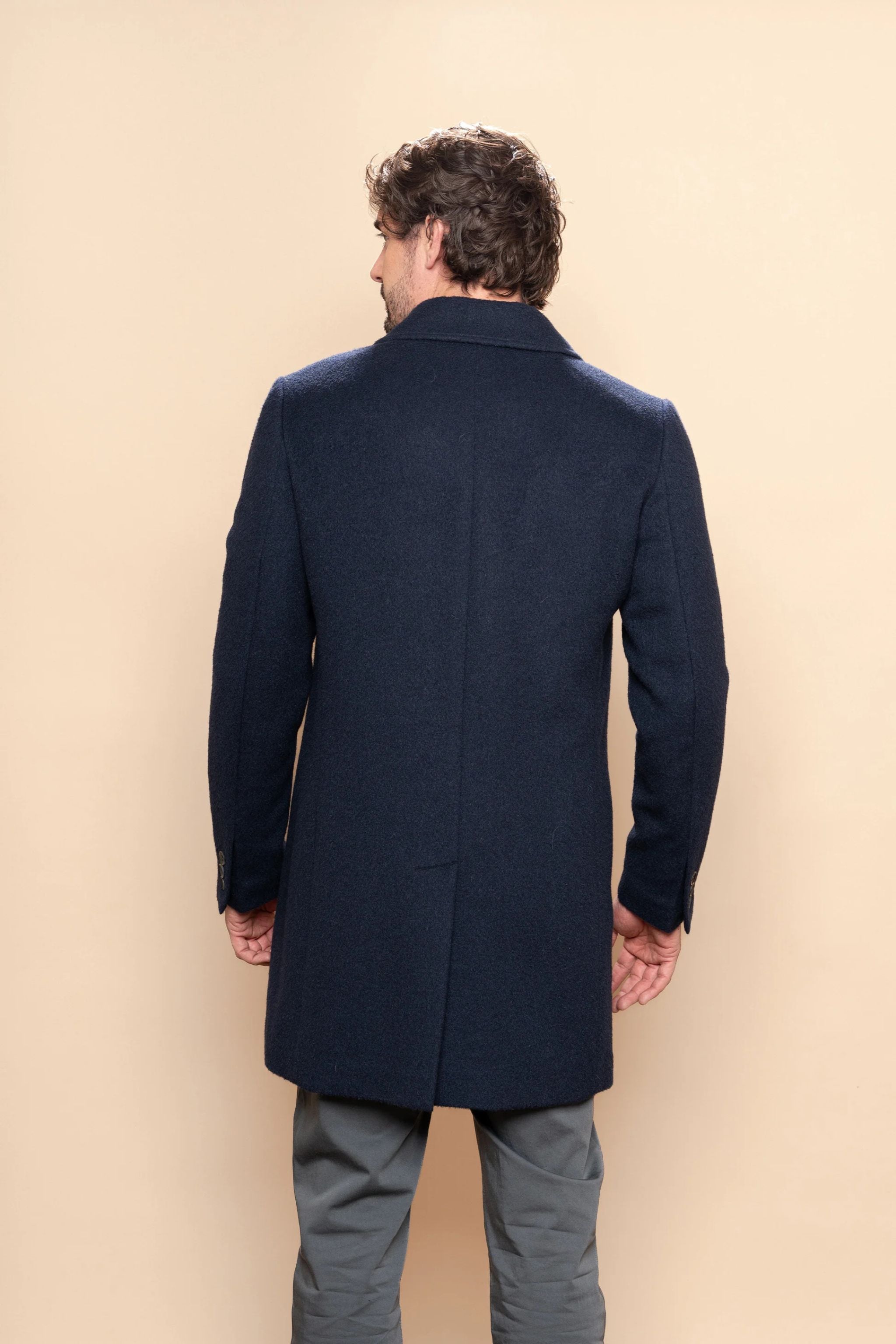 Man wearing a navy blue coat against a beige background