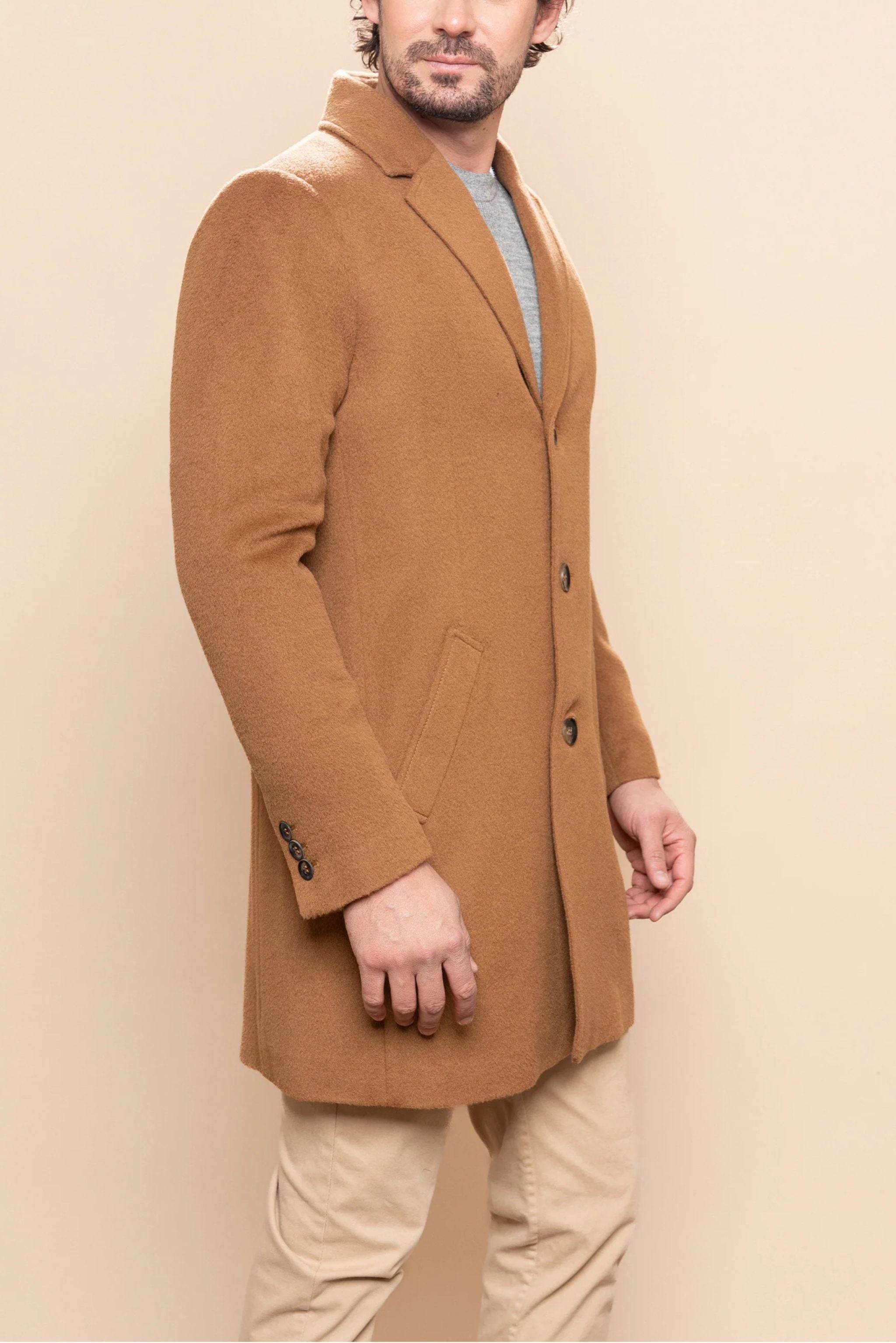 Man wearing a brown coat against a beige background