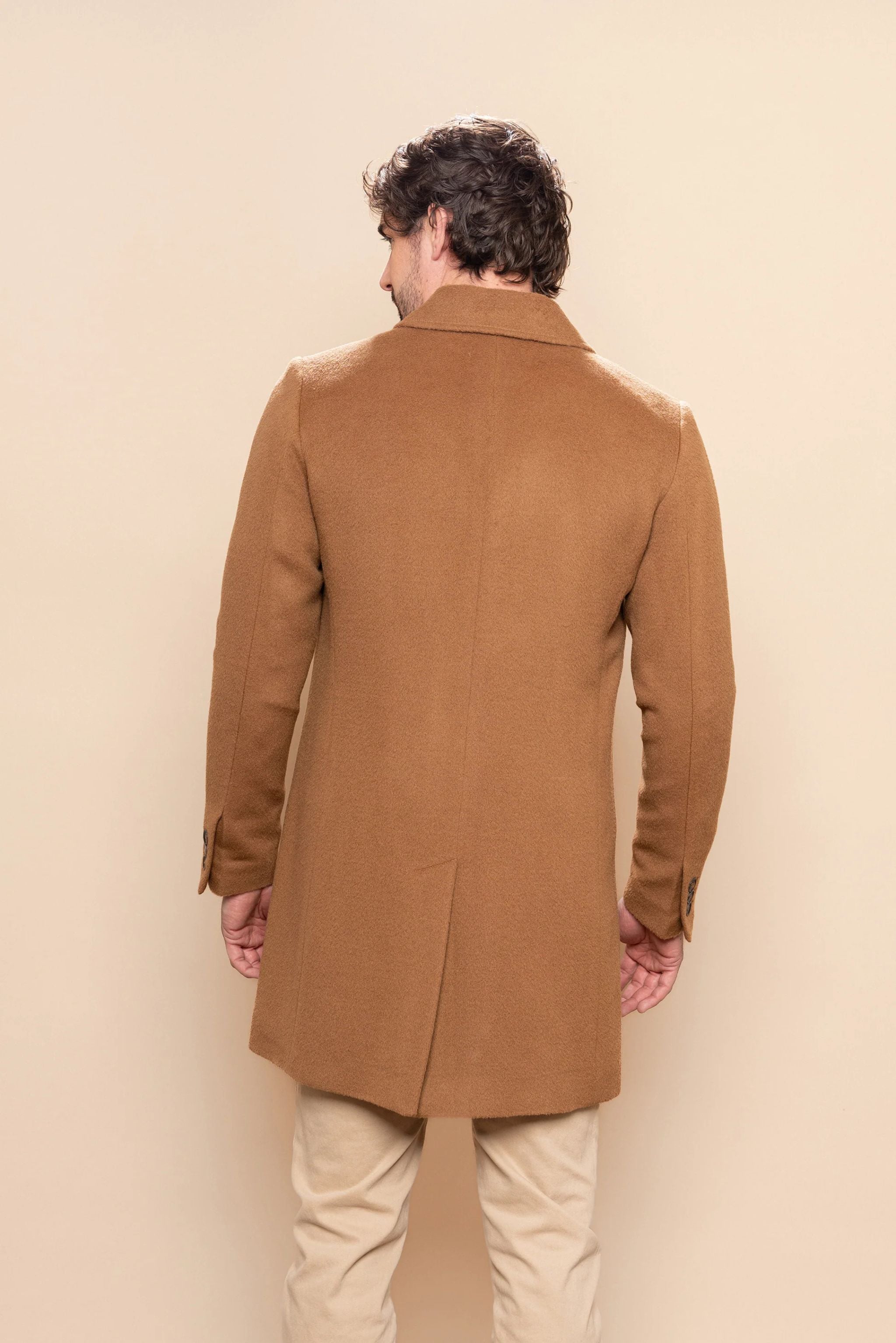 Man wearing a brown coat against a beige background