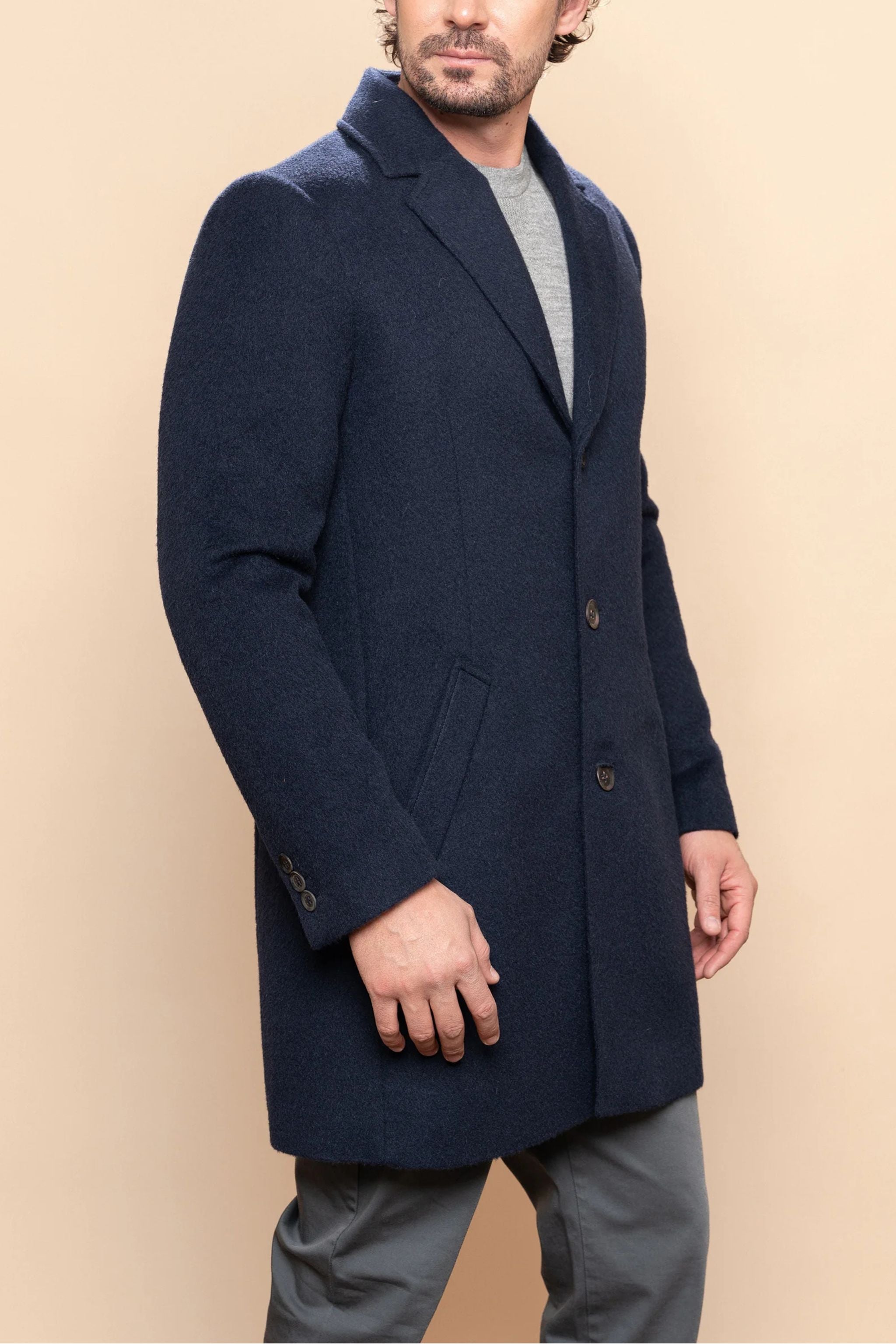 Man wearing a navy blue coat against a beige background